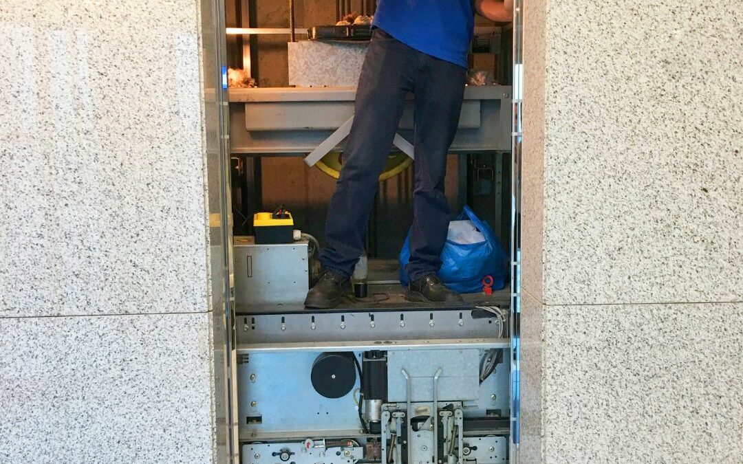 A Pincus Elevator Company technician repairing an elevator with its door open and operating machinery exposed.