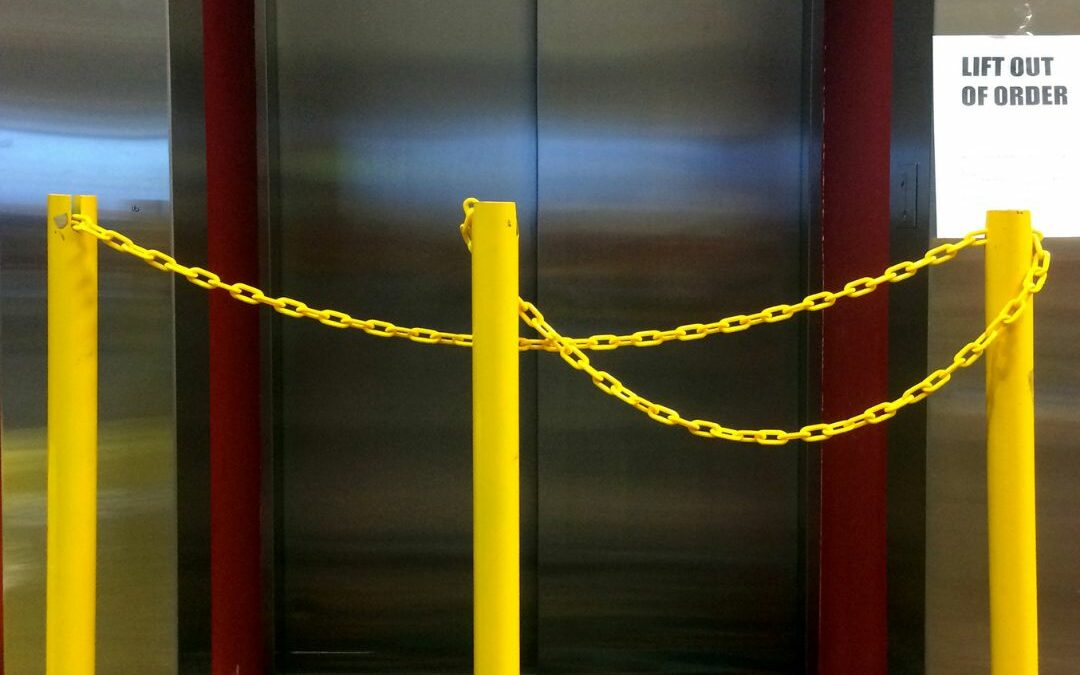 Yellow stations with ropes blocking access to an out of service elevator that needs modernized.
